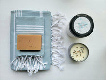 Load image into Gallery viewer, Light Blue set of Turkish bath and hand towels with tassels, a bar of soap, a eucalyptus mint bath salts, and a lavender sage candle on a white background.
