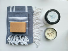 Load image into Gallery viewer, Navy set of Turkish bath and hand towels with tassels, a bar of soap, a eucalyptus mint bath salts, and a lavender sage candle on a white background.