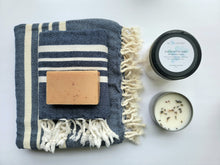 Load image into Gallery viewer, Navy set of Turkish bath and hand towels with tassels, a bar of soap, a eucalyptus mint bath salts, and a lavender sage candle on a white background.